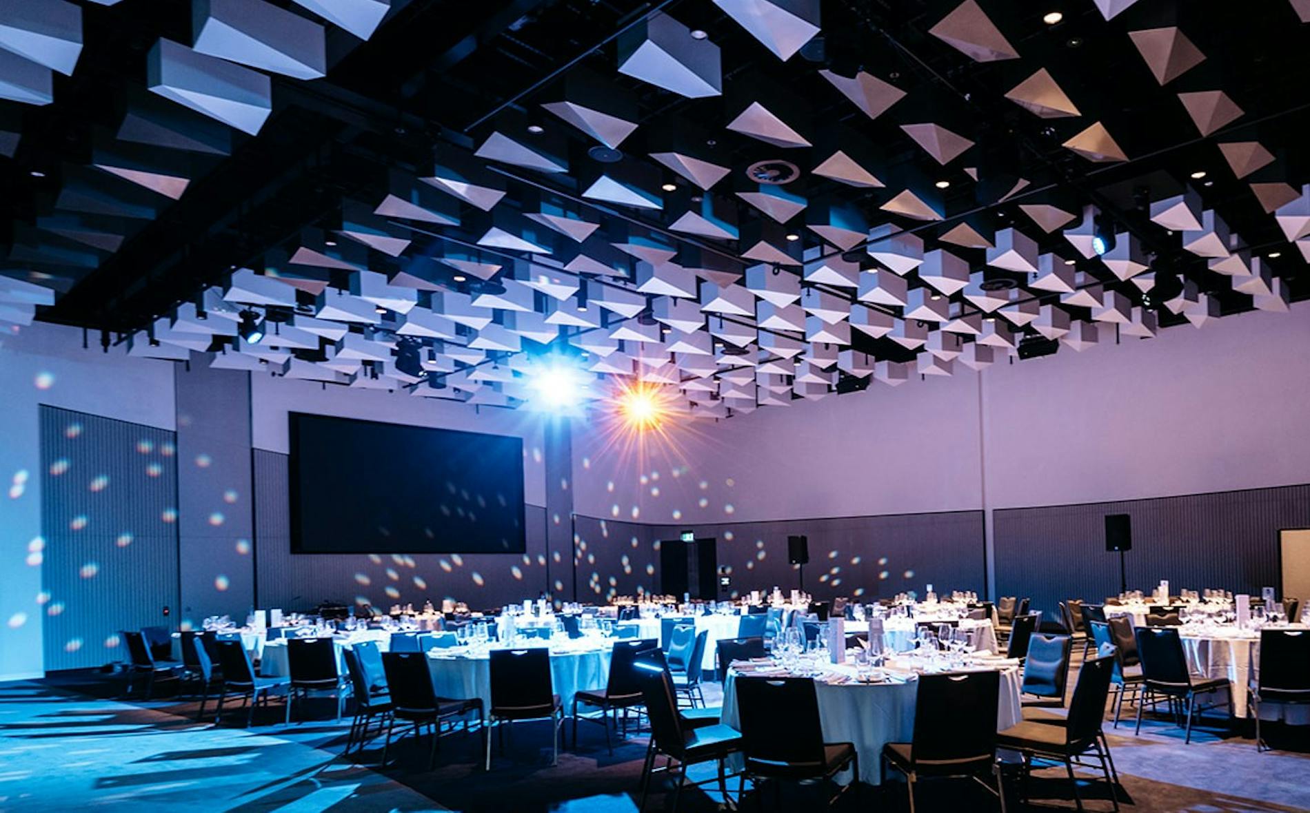 Te Pae features an elegantly arranged dining space with round tables set for guests. Soft lights illuminate the modern design, creating a vibrant atmosphere for gatherings.